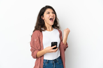 Fototapeta premium Teenager Russian girl isolated on white background with phone in victory position