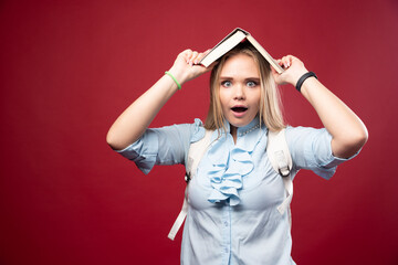 Young blonde schoolgirl holds her book at her head and looks tired and confused
