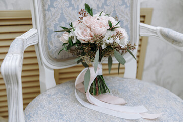 A wedding bouquet of white roses in an expensive interior lies on a chair,festive ribbons on the bouquet, details at the wedding, the bride's bouquet