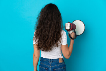 Teenager Russian girl isolated on blue background holding a megaphone and in back position