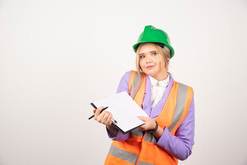 Young female contractor with green helmet opened clipboard on white background