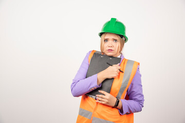 Young female contractor with green helmet and clipboard on white background
