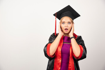 Female student in gown holding her face on white background