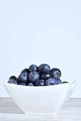 Blueberries in porcelain bowl, light background and copy space.