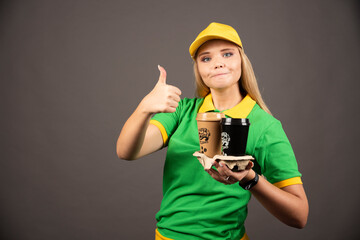 Deliverywoman holding cups of coffee and showing thumb up