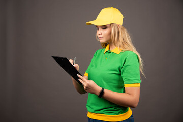 Young female courier with pencil looking on clipboard