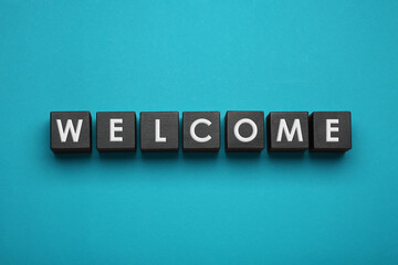 Word Welcome made of black cubes with letters on turquoise background, top view