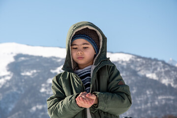 The boy stands in the winter in a green jacket against the backdrop of the mountains