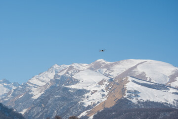 Fototapeta na wymiar Quadcopter drone flies against the backdrop of snow-capped mountains and blue sky