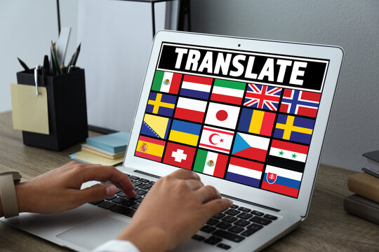 Translator using modern laptop with images of different flags on screen at table in office, closeup