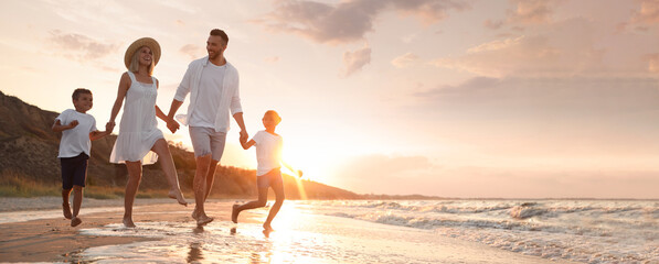 Happy family running on sandy beach near sea at sunset, space for text. Banner design - Powered by Adobe