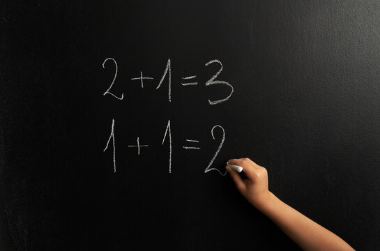 Image of little boy's hand who  is solving a math equation on the chalk board.