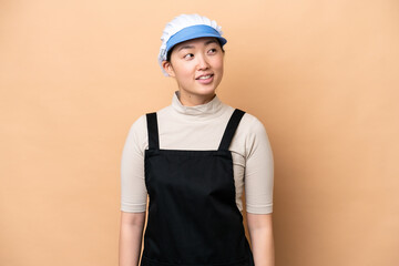 Young Chinese Fishmonger woman wearing an apron and holding a raw fish isolated on pink background looking to the side and smiling