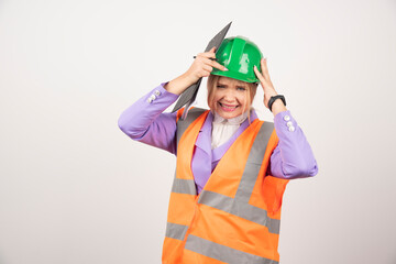 Young female contractor with green helmet and clipboard on white background