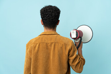 Young Moroccan man isolated on blue background holding a megaphone and in back position