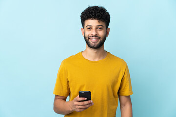 Young Moroccan man isolated on blue background using mobile phone