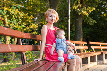 beautiful mother with her daughter and son are sitting on a bench in the park in the summer