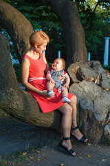 beautiful mother with a son sit on a tree in the park in summer