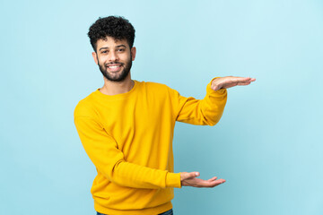 Young Moroccan man isolated on blue background holding copyspace to insert an ad