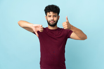 Young Moroccan man isolated on blue background making good-bad sign. Undecided between yes or not