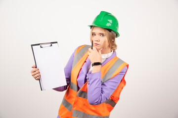 Young female contractor with green helmet and clipboard on white background