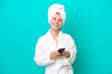 Young woman in a bathrobe isolated on blue background sending a message with the mobile