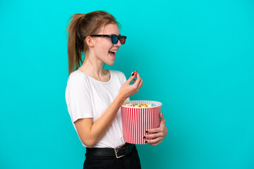 Young English woman isolated on blue background with 3d glasses and holding a big bucket of...
