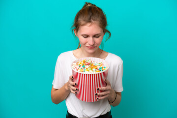 Young English woman isolated on blue background holding a big bucket of popcorns