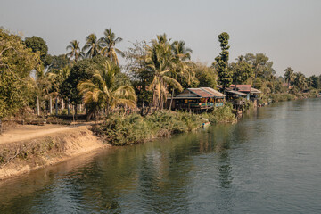 View on the Mekong River from Don Det Island in the south of Laos on a sunny day with palm trees and houses on the banks of the river.