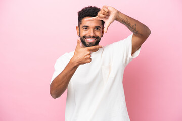 Young Brazilian man isolated on pink background focusing face. Framing symbol
