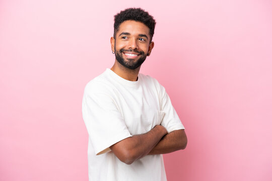 Young Brazilian man isolated on pink background with arms crossed and happy