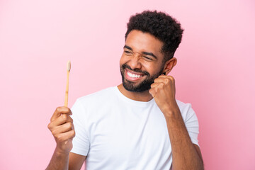 Young Brazilian man brushing teeth isolated on pink background celebrating a victory