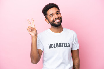 Young volunteer man isolated on pink background smiling and showing victory sign