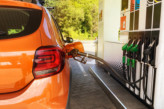 Fill car with fuel in petrol station. Pumping gasoline fuel in orange car at a gas station in city.