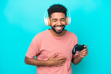 Young brazilian man playing with a video game controller isolated on blue background smiling a lot