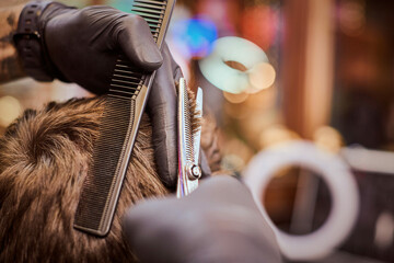 Male haircut in barbershop close up, client getting haircut by hairdresser with comb and scissors