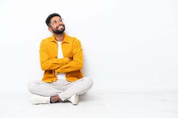 Young Brazilian man sitting on the floor isolated on white background looking up while smiling