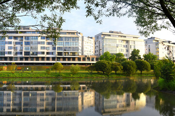 Facade building at lake. Modern residential building at river. Design of facade of a multi-storey home with windows and balconies. Penthouse and Townhouse on lake in the city park.