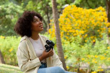 happy african american beautiful woman holding binoculars In a park with many trees. Birdwatching. Birdwatching. Look for something with binoculars.