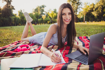 Portrait of attractive cheerful girl lying on cover using laptop writing plan home task exercise...