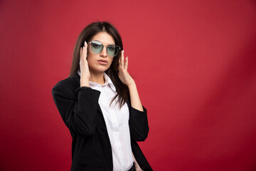 Young businesswoman posing with glasses on red background