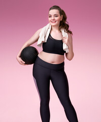 Sporty girl resting after training. Photo of pretty model with curvy figure in black sportswear on pink background. Sports motivation and healthy lifestyle