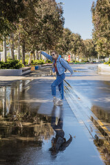 A woman in a street denim outfit dances in a wet park alley reflected in a puddle. Spring joy after the rain