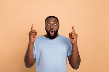 Portrait of attractive amazed wondered guy pointing up copy space isolated over beige pastel color...
