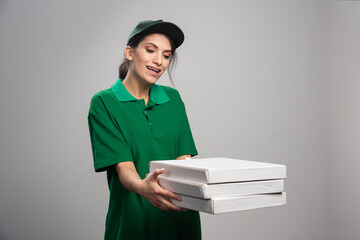 Young female courier posing with pizza boxes on gray background