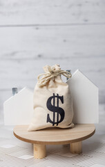 A money bag and a wooden house symbolizing the rising costs of housing and the real estate market due to inflation in the economy