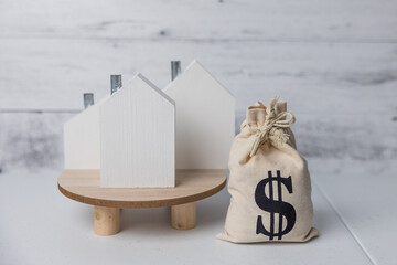 A money bag and a wooden house symbolizing the rising costs of housing and the real estate market due to inflation in the economy