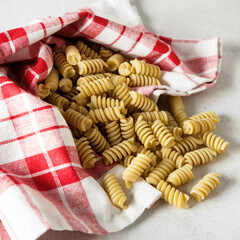 Uncooked Fusilli Pasta with a Linen Napkin on a Gray Background Square