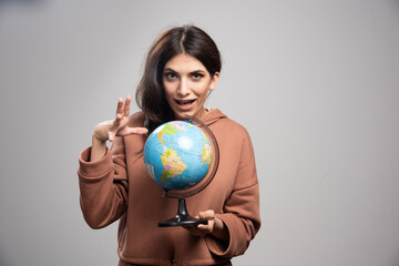 Brunette woman holding globe on gray background