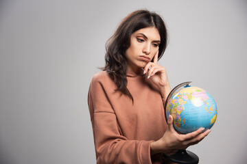 Serious looking woman looking at globe on gray background